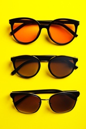 Many stylish sunglasses on yellow background, flat lay