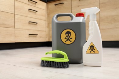 Bottles of toxic household chemicals with warning signs and brush on floor indoors, space for text