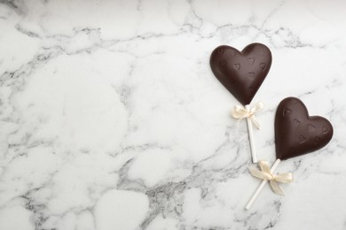Chocolate heart shaped lollipops on white marble table, flat lay. Space for text