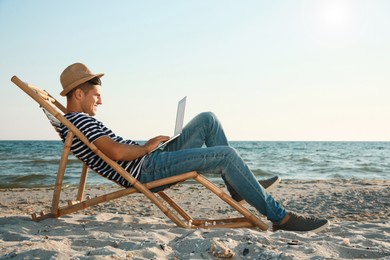 Man working with laptop in deck chair on beach