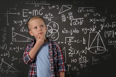 Thoughtful little boy near chalkboard with different formulas