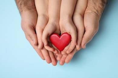Photo of Parents and kid holding red heart in hands on light blue background, top view