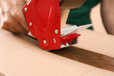 Man packing box with adhesive tape, closeup. Moving service