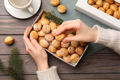 Photo of Woman taking delicious nut shaped cookies from box at wooden table, top view