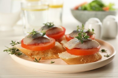 Delicious sandwiches with salted herring, tomatoes and thyme on light beige table, closeup