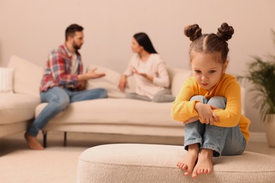 Photo of Sad little girl and her arguing parents on sofa in living room