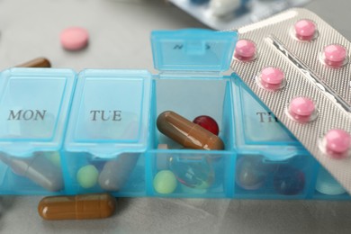 Plastic box with different pills on light grey stone table, closeup