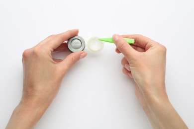 Photo of Woman taking contact lens from case with tweezers on white background, top view