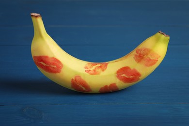 Banana covered with red lipstick marks on blue wooden table. Potency concept