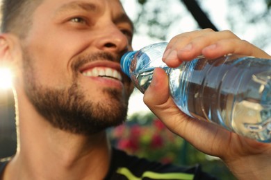Happy man drinking water outdoors on hot summer day, closeup. Refreshing drink