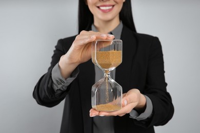 Businesswoman holding hourglass on light grey background, closeup. Time management
