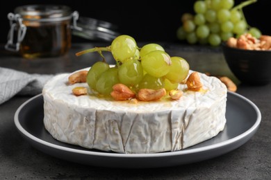 Brie cheese served with grape, cashew nuts and honey on dark grey table, closeup