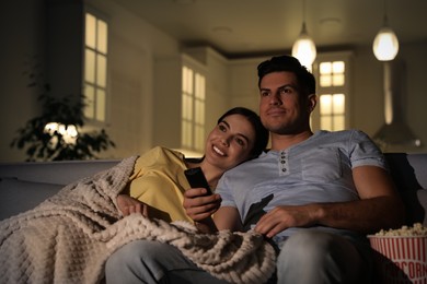 Couple watching movie with popcorn on sofa at night