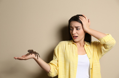 Scared young woman holding tarantula on beige background. Arachnophobia (fear of spiders)