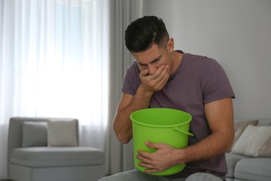 Man with bucket suffering from nausea at home, space for text. Food poisoning