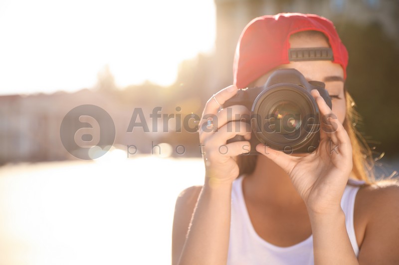 Photo of Young photographer taking picture with professional camera outdoors. Space for text