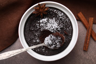 Photo of Tasty powdered chocolate pie with anise and spoon on brown table, flat lay. Microwave cake recipe