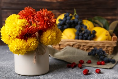 Photo of Bouquet of beautiful chrysanthemum flowers, rose hip berries and sweet fruits on grey table. Space for text