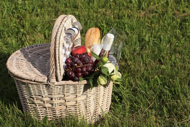 Picnic basket with tasty food, flowers and cider on grass. Space for text