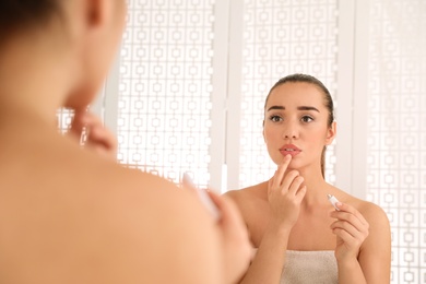 Photo of Woman with herpes applying cream on lips in front of mirror at home