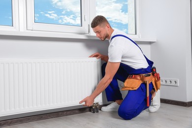 Professional plumber installing new heating radiator in room