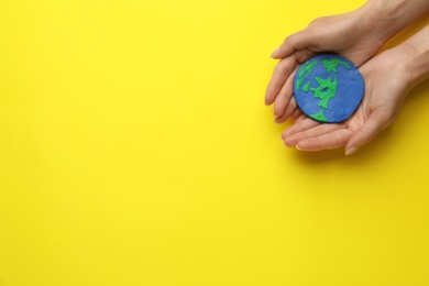 Woman holding plasticine model of planet on yellow background, top view with space for text. Earth Day