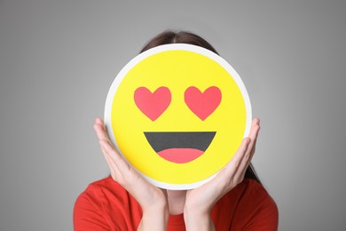 Photo of Woman covering face with heart eyes emoji on grey background