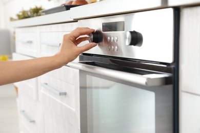 Photo of Woman regulating cooking mode on oven panel in kitchen, closeup