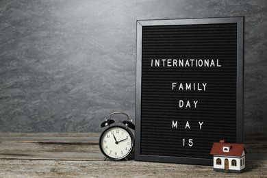 Photo of Happy Family Day. Black letter board with text, clock and house model on wooden table. Space for design