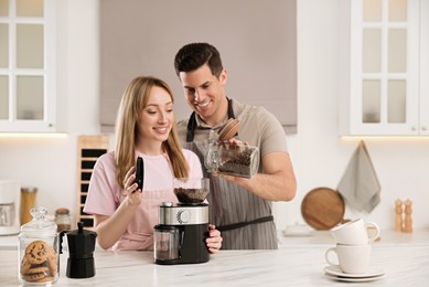 Lovely couple using electric coffee grinder together in kitchen