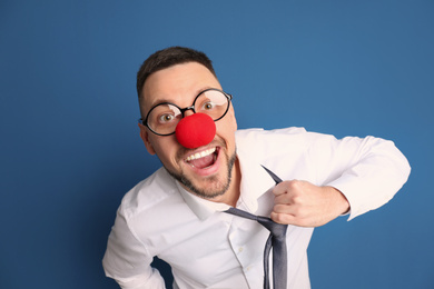 Joyful man with glasses and clown nose on blue background. April fool's day