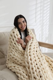 Young woman with chunky knit blanket on sofa at home