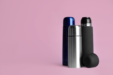 Stylish thermo bottles on pink background, space for text