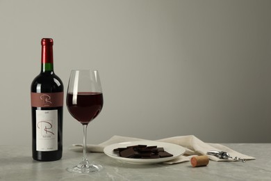 Bottle and glass of red wine with chocolate on light marble table. Space for text