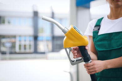 Young worker with fuel pump nozzle at modern gas station, closeup