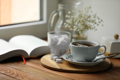 Tray with cup of freshly brewed tea and sugar cubes on wooden table, space for text