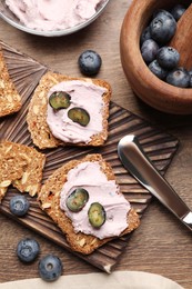 Tasty sandwiches with cream cheese and blueberries on wooden table, flat lay