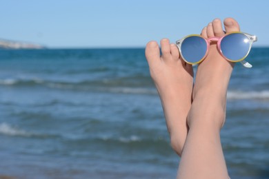 Photo of Child resting near sea, closeup of feet with sunglasses. Space for text