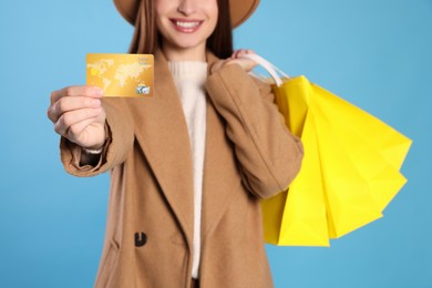 Photo of Woman holding shopping bags and credit card on light blue background, closeup