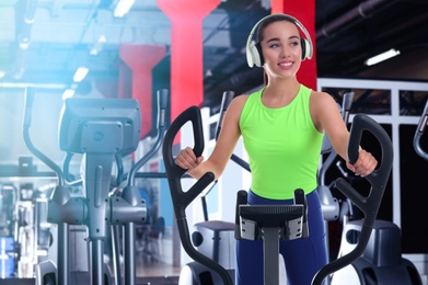 Woman with headphones using modern elliptical machine in gym