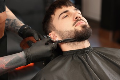 Professional hairdresser working with bearded client in barbershop, closeup