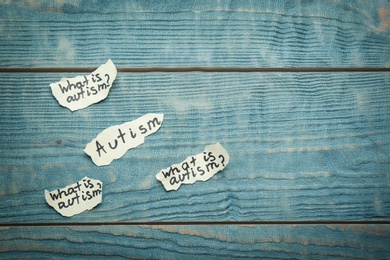 Paper pieces with phrases about autism on wooden background