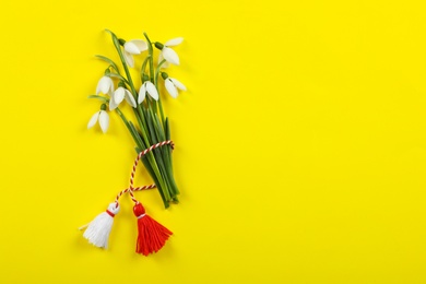 Beautiful snowdrops with traditional martisor on yellow background, flat lay and space for text. Symbol of first spring day
