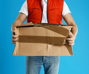 Courier with damaged cardboard box on blue background, closeup. Poor quality delivery service