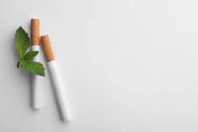 Menthol cigarettes and fresh mint leaves on white background, flat lay. Space for text