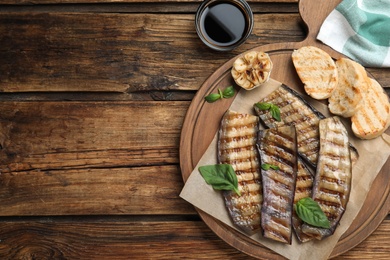 Delicious grilled eggplant slices served on wooden table, flat lay. Space for text