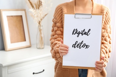 Photo of Woman holding clipboard with phrase DIGITAL DETOX at home, closeup. Space for text