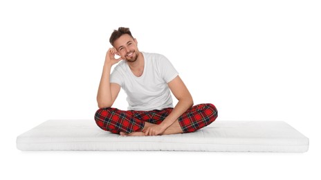 Smiling man sitting on soft mattress against white background