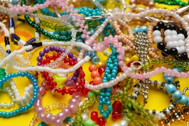 Pile of beautiful handmade beaded jewelry on yellow background, closeup