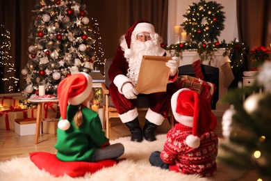 Santa Claus with wish list and children in room decorated for Christmas